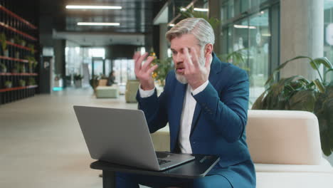 angry mature boss arguing over video call using laptop while sitting at modern workplace in office