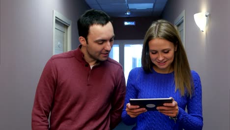 una pareja joven caminando por el pasillo del hotel con una mujer sonriente sosteniendo una tableta