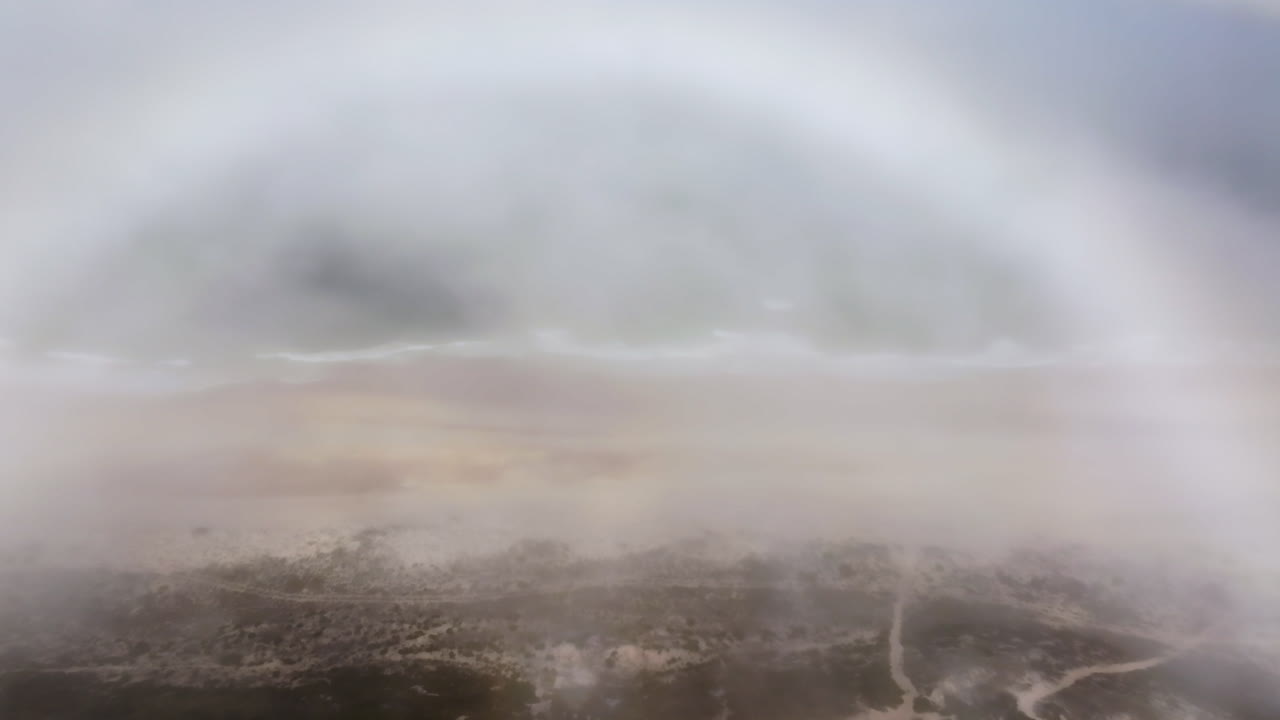 vista aérea de una playa brumosa con un arco iris