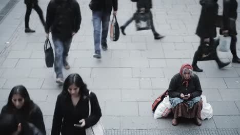 amid a bustling city, a woman sits quietly on the pavement, absorbed in her phone.