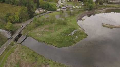 Multiple-car's-driving-across-a-small-bridge-at-the-end-of-a-stream,-ascending-aerial