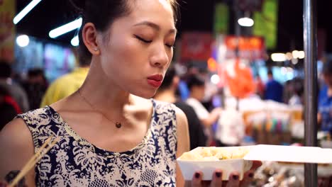 mujer asiática comiendo dumplings fritos en el mercado nocturno