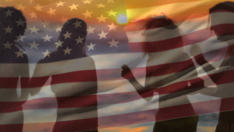 group of friends dancing in the beach and an american flag for fourth of july.