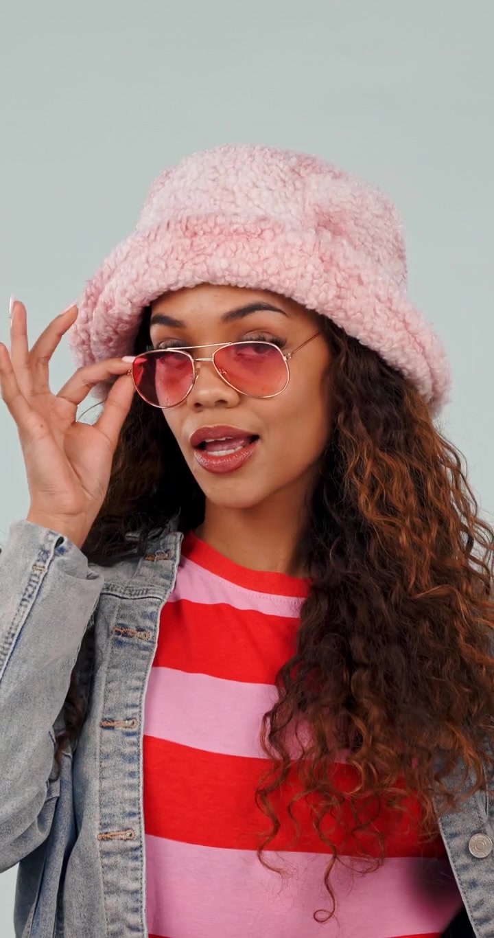 Elegante giovane donna che indossa un cappello bucket rosa e occhiali da sole in posa