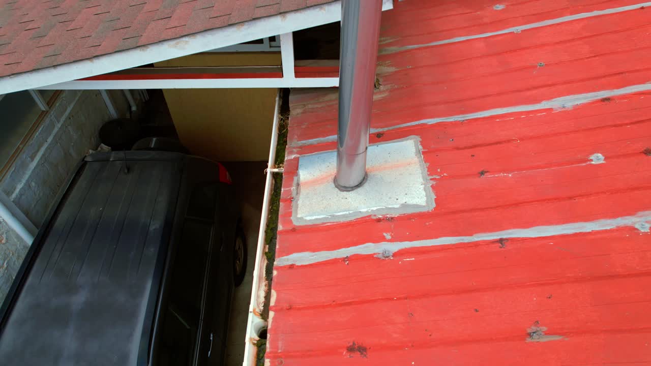 A red metal roof with chimney pipe and a parked car below in vina del mar, chile, aerial view