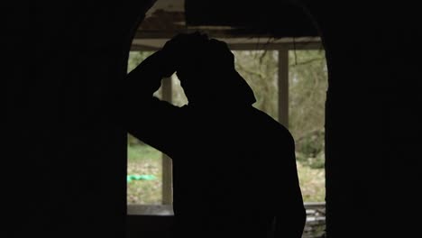 Silhouette-portrait-of-young-man-inside-abandoned-mansion,-standing-in-the-corridor-in-front-of-big-window