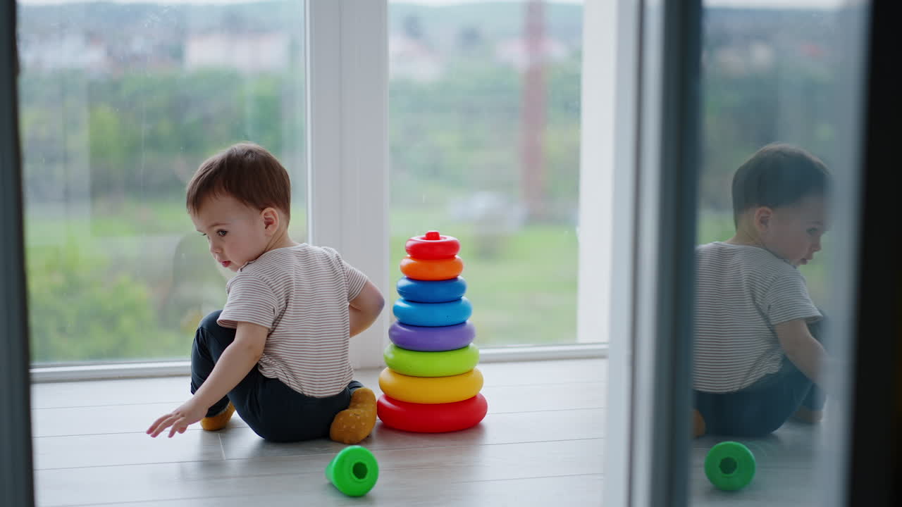 Baby boy assembled the colorful toy pyramid. Kid wants to take the top but distracts on something and moves back.