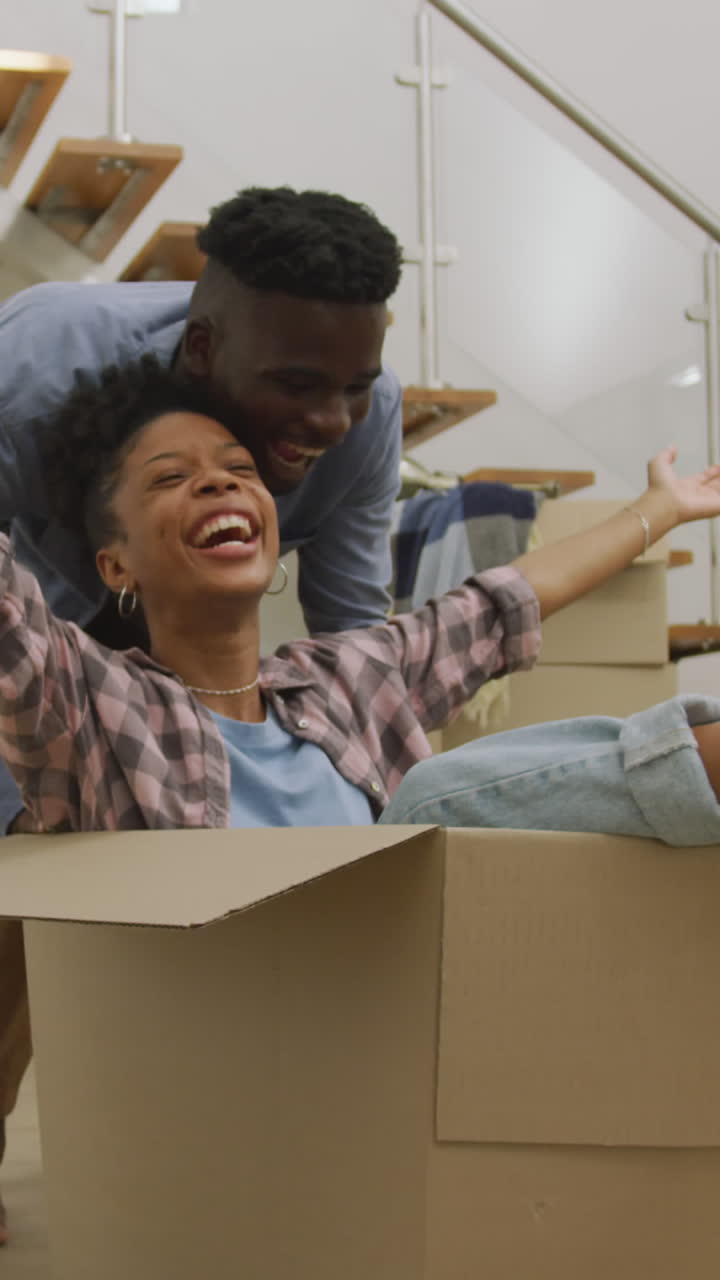 video de una feliz pareja afroamericana divirtiéndose con cajas después de mudarse a una casa nueva