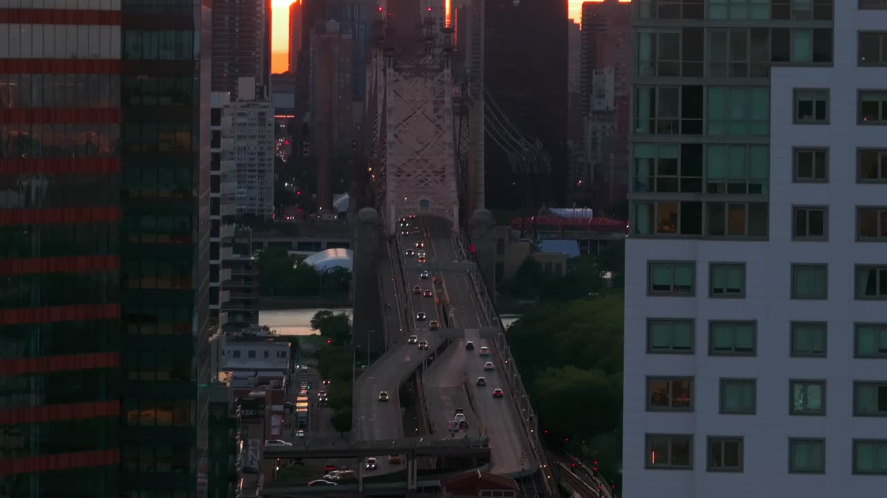 An aerial shot of the Queensboro Bridge, seen from Long Island City between skyscrapers in Queens during a golden sunset. The drone camera dolly out slowly.