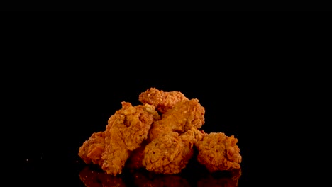 golden, crumbed spicy chicken pieces are slowly zoomed in on against a black background, highlighting crispy texture and vibrant color under dramatic lighting