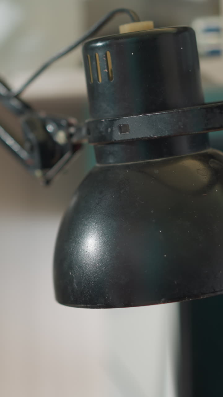 A close-up view of a technician's hand in a black glove adjusting a lamp, with a blurred background showing a shelf