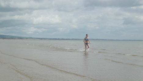 trajes de baño, salpicaduras de agua de mar, joven y hermosa chica corriendo, en cámara lenta