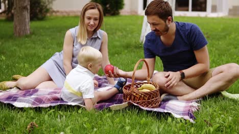 happy family sitting on a plaid at the picnic on the green beautiful meadow on a sunny day. their son is sitting near. enjoy the picnic. outdoors