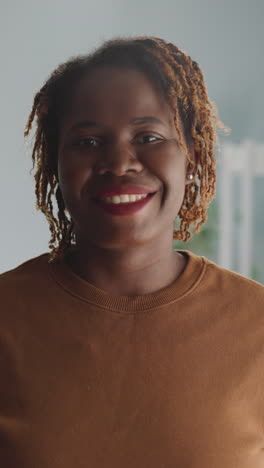 positive african american woman shows friendly attitude standing against bright lamp at home. portrait of lady looking in camera with white-toothed smile closeup