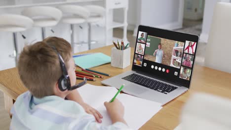 schoolboy using laptop for online lesson at home, with diverse teacher and class on screen