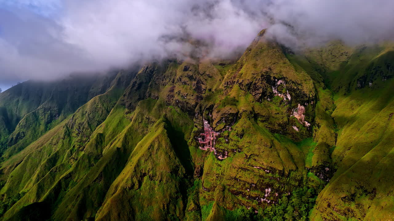 Aerial shot with the drone flying closer to the majestic, mist-covered green mountains of Bukit Selong