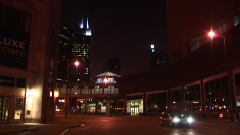 Nächtliche-Urbane-Szene-Mit-Taxis-Und-Anderen-Fahrzeugen,-Die-über-Eine-Kreuzung-Mit-Dem-Wahrzeichen-Von-Chicago-Fahren,-Dem-Sears-Tower-Im-Hintergrund