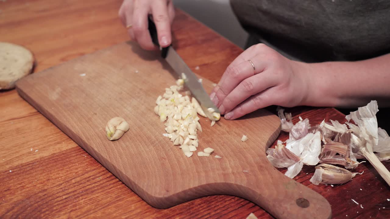 Woman's hands with a knife chops garlic on a chopping board