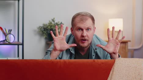 man playing hide and seek peekaboo game hiding behind sofa looking at camera, positive smiling