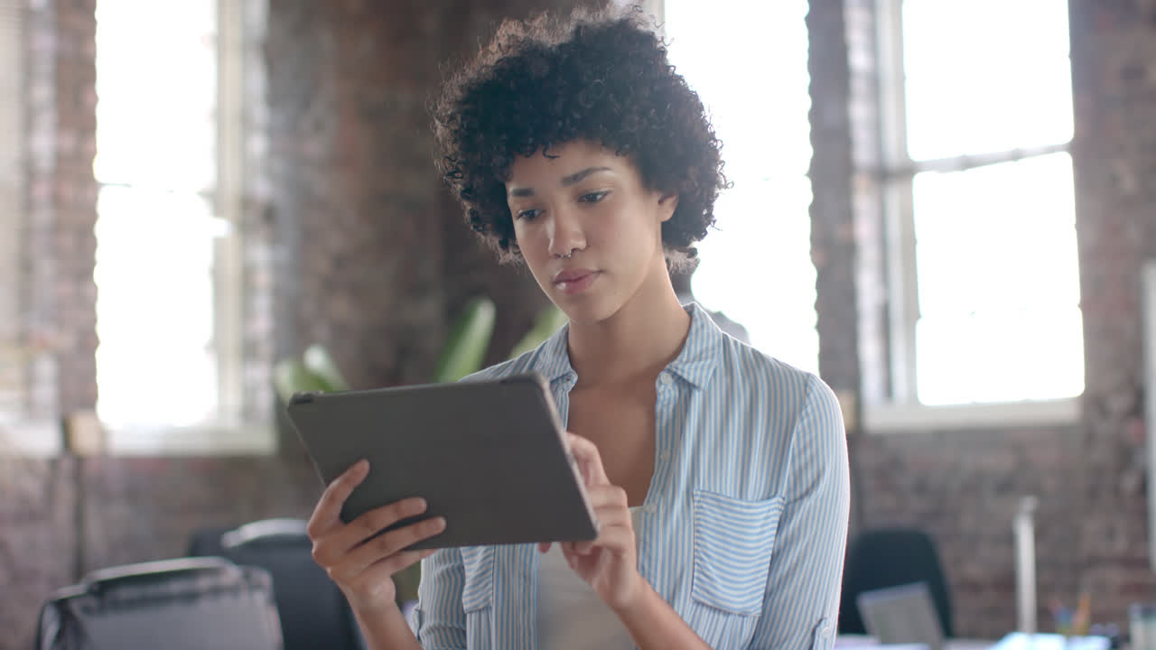 Portrait of happy biracial casual businesswoman using tablet in office in slow motion
