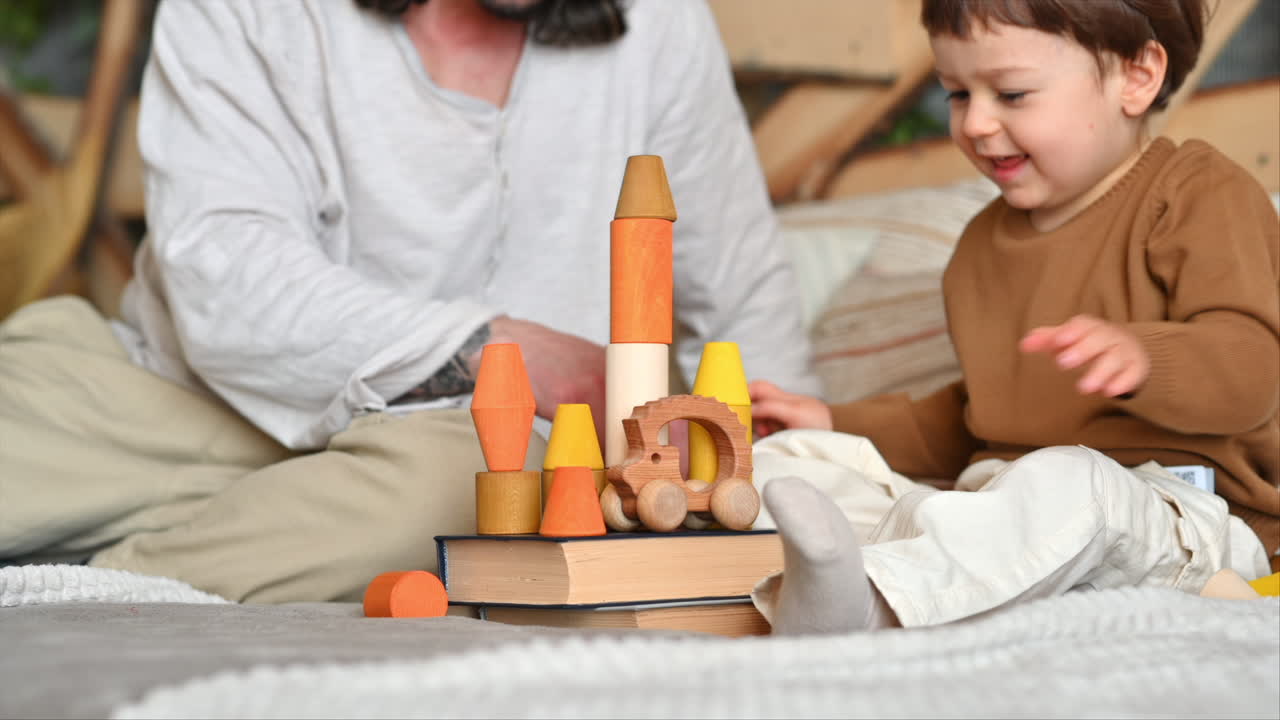 Father playing with his son with colourful, ecological wooden toys on the bed
