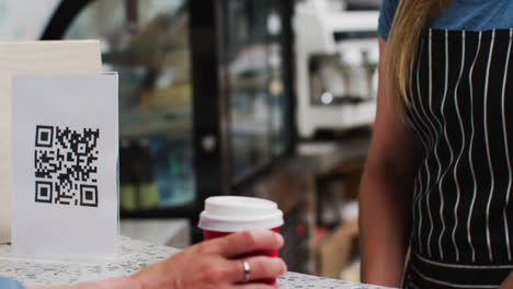 Mid-section-of-woman-wearing-face-mask-making-payment-using-smartwatch-at-a-cafe