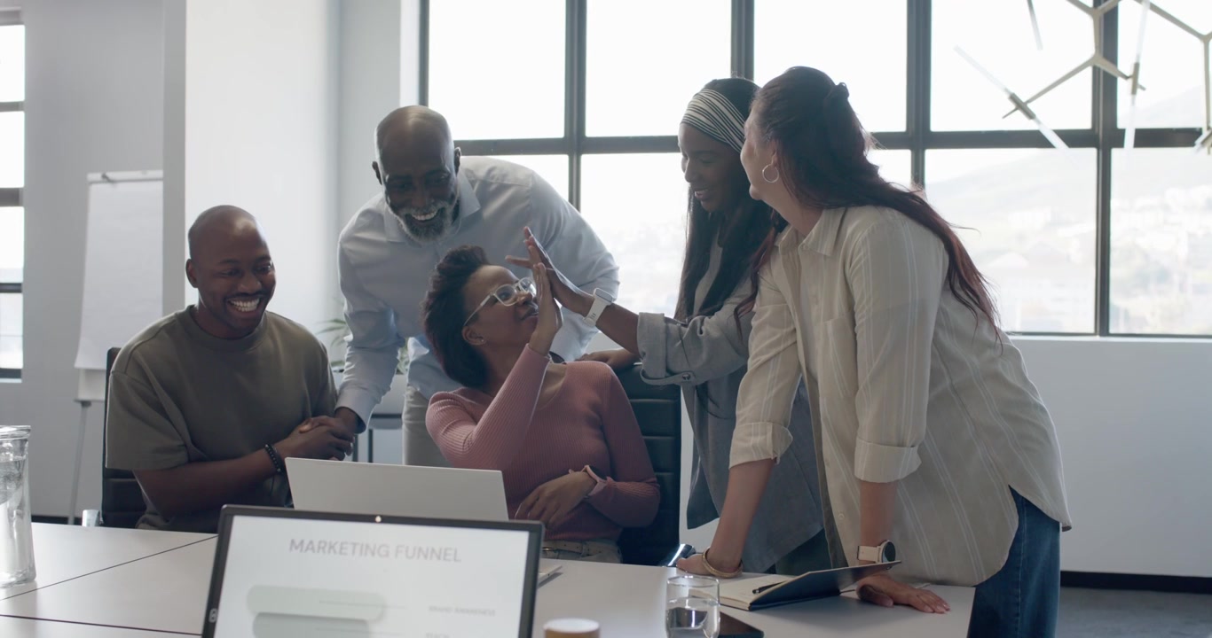 Diverse team in office cheering around woman with glasses at laptop reacting to MARKETING FUNNEL