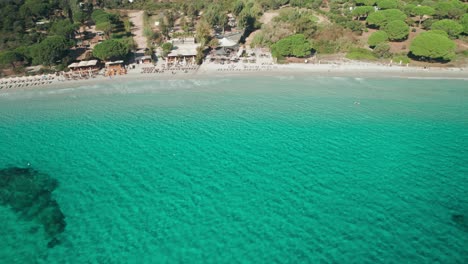 aerial, drone footage of a beach with deckchairs and turquoise water, corsica
