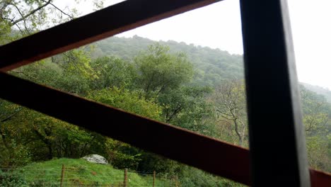 Raining-weather-in-rural-mountain-countryside-through-rustic-oak-wood-barn-planks-opening