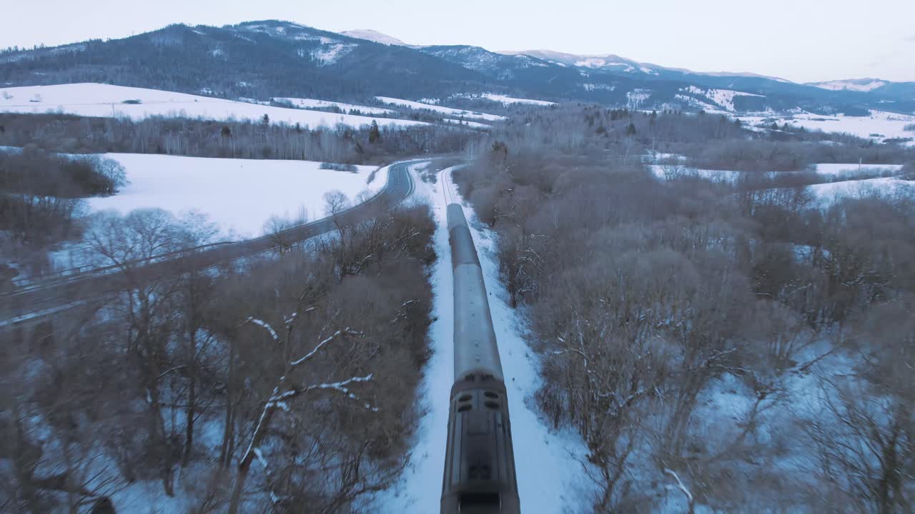 Incredible aerial drone view of fast moving train travelling in snowy magical white landscape, dusk, circle pan, Slovakia High Tatra winter landscape