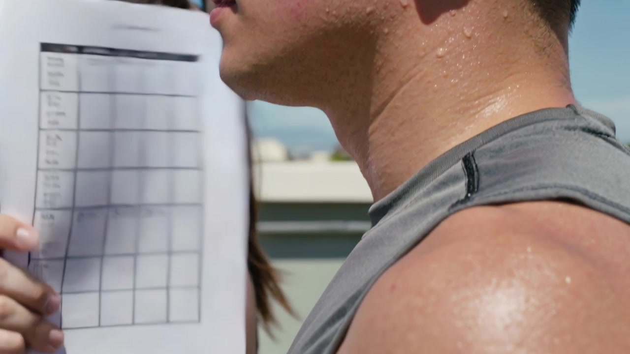 Waving female moving grid paper across male sleeveless top on rooftop shading sun, copy space