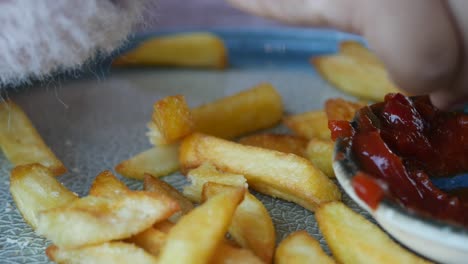 child's hand reaching for french fries with ketchup