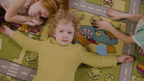 Top-View-Of-A-Little-Boy-Lying-On-The-Carpet-With-Open-Arms-And-Looking-At-Camera-1