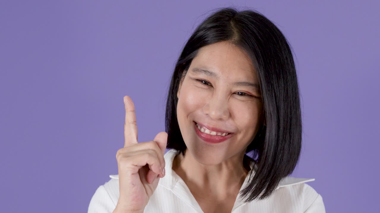紫色の背景を前に、アジア人女性が物思いにふける表情から、ひらめきを得て喜ぶジェスチャーへと変わる。