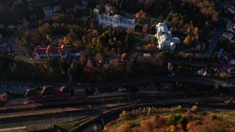 Aerial-shot-of-autumnal-forest-by-railway-and-Sinaia-landmarks,-golden-hour-light,-tranquil-mood,-distant-mountains