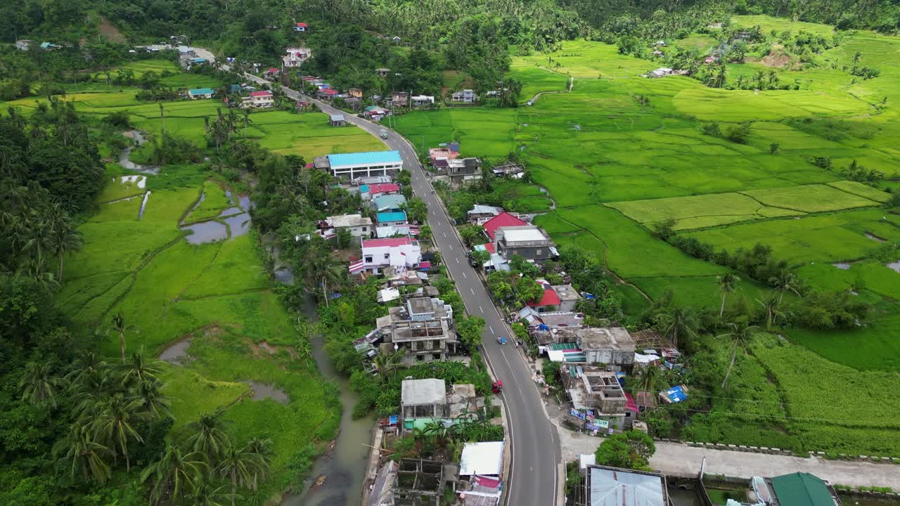 Bato town road curving through green hills and clustered rooftops in Catanduanes Philippines, aerial tracking along road