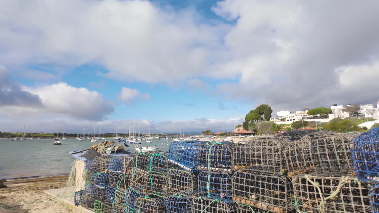Stacked fishing cages at Alvor harbour with boats and white buildings Portugal Algarve