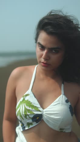 young woman at beach in floral bikini, looking serious, wind in hair, soft focus look