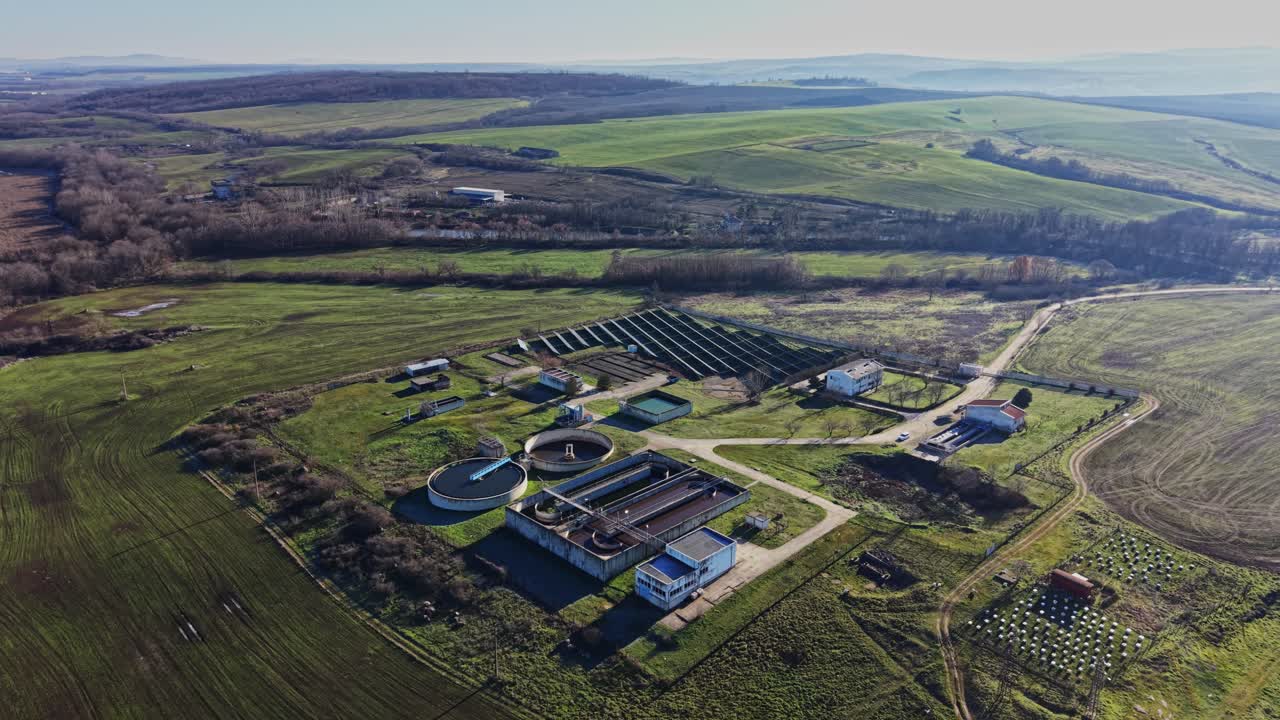 View over a large field with water treatment facilities and green hills