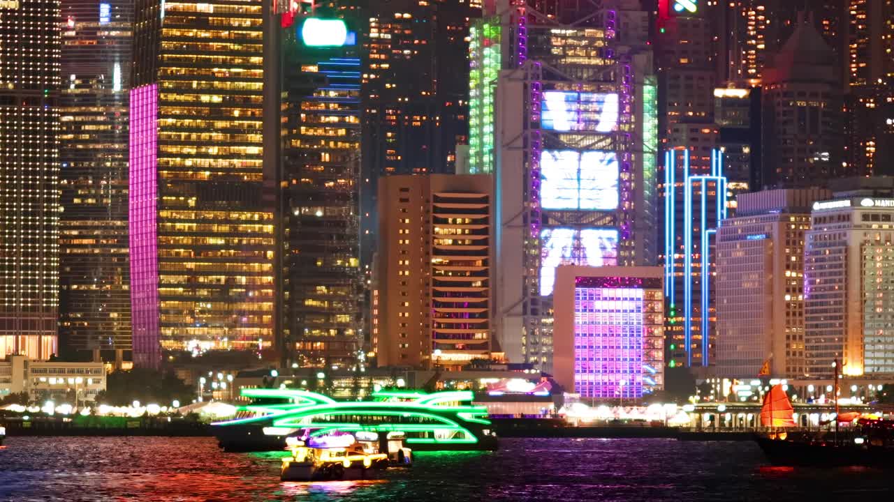 Colorful skyscraper lights illuminate the waterfront with vibrant reflections and dynamic patterns.