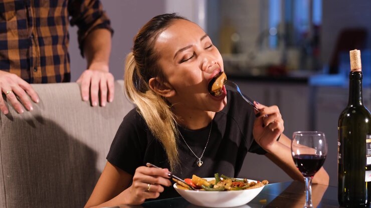 Asian girl is greedily eating her dinner. She appears very hungry as she swallows the food.Her husband is standing behind her after serving the food.