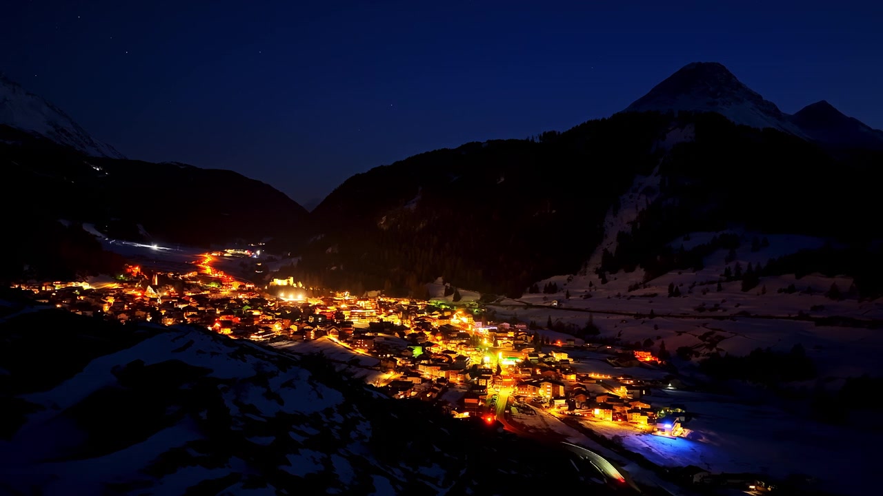 Villaggio montano di Nauders, Austria, che risplende di luci calde sotto un cielo notturno scuro in un timelapse aereo