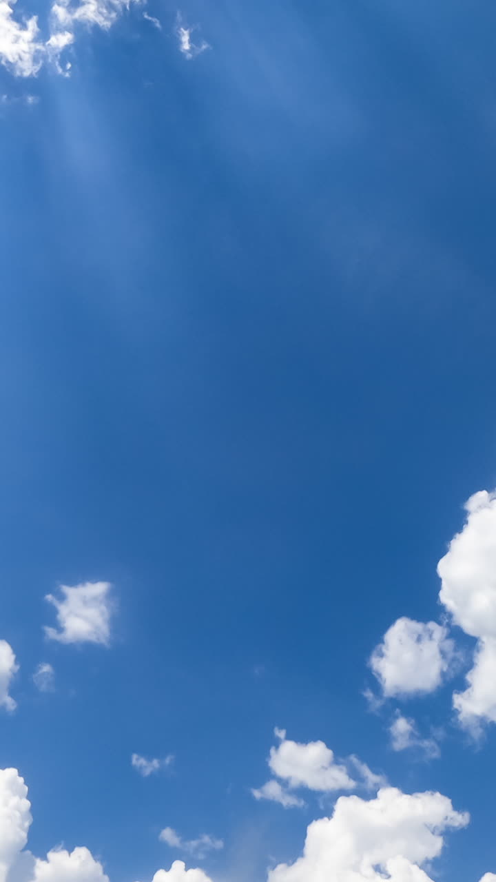 Beautiful sunrays coming through the light soft clouds in the blue summer sky. Timelapse low angle view. Vertical video