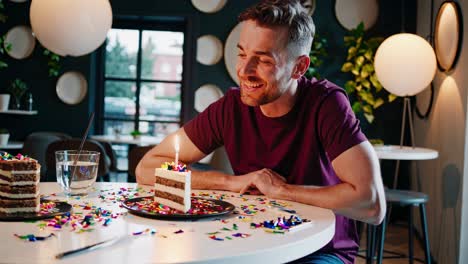 montage of a happy man sitting at a table in a modern cafe, smiling and looking at a slice of birthday cake with a lit candle and colorful confetti