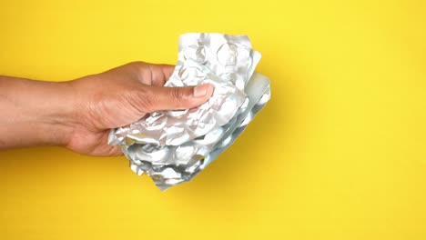 hand holding crumpled aluminum foil pill packaging on yellow background
