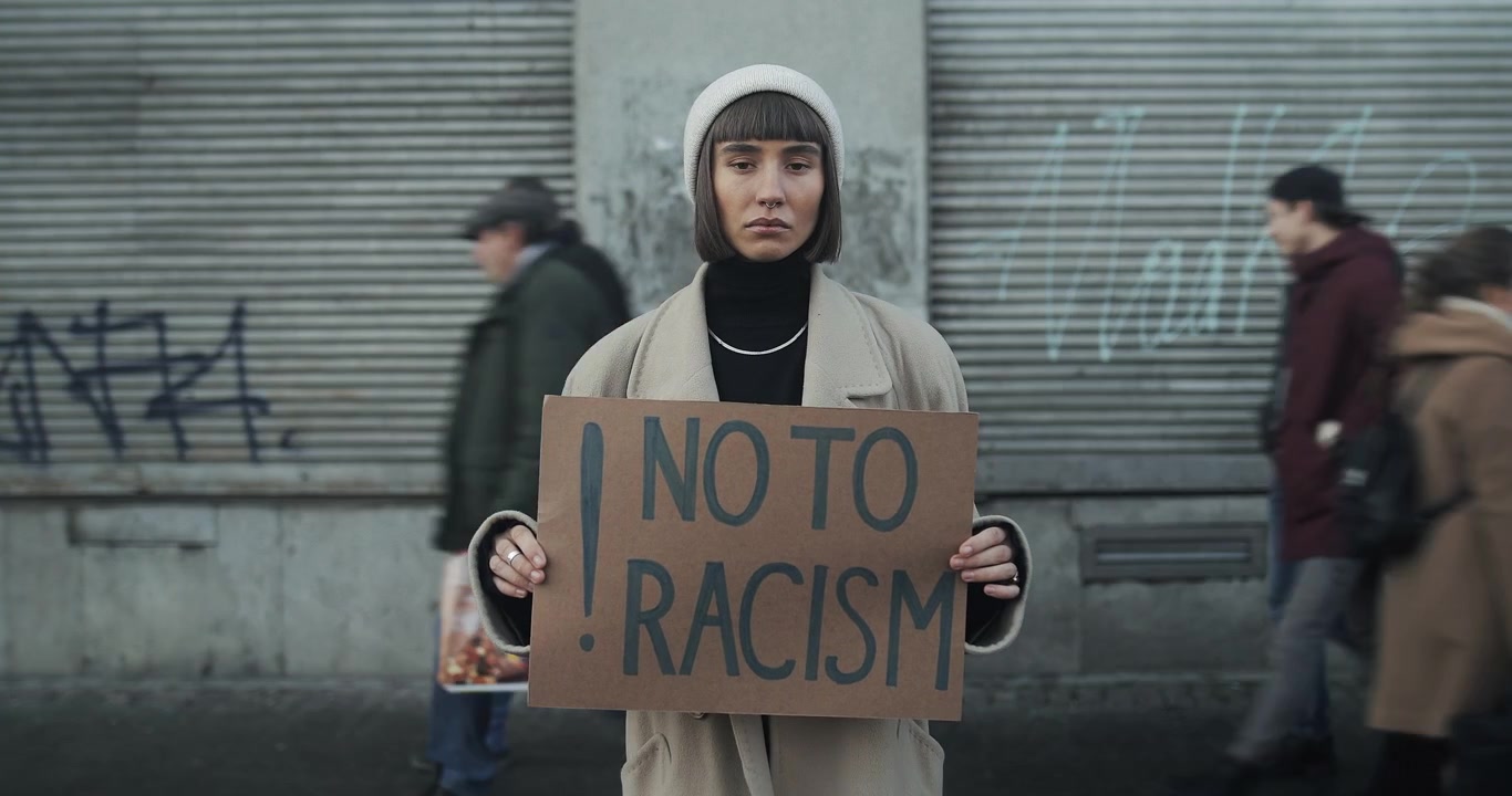 Giovane donna che tiene un cartello contro il razzismo in una trafficata strada cittadina