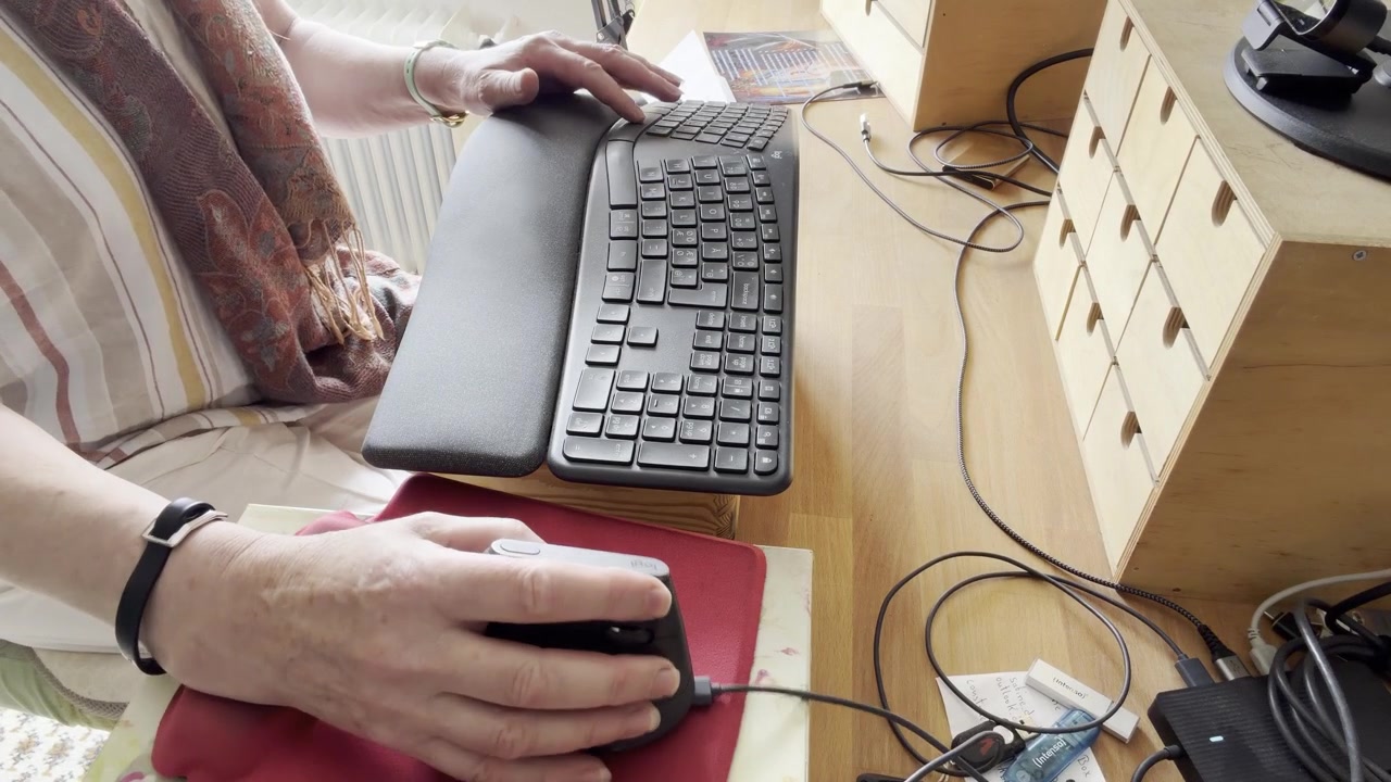 Mani femminili che muovono un mouse del computer su un tappetino rosso mentre digitano su una tastiera ergonomica su una scrivania di legno. Inquadratura fissa