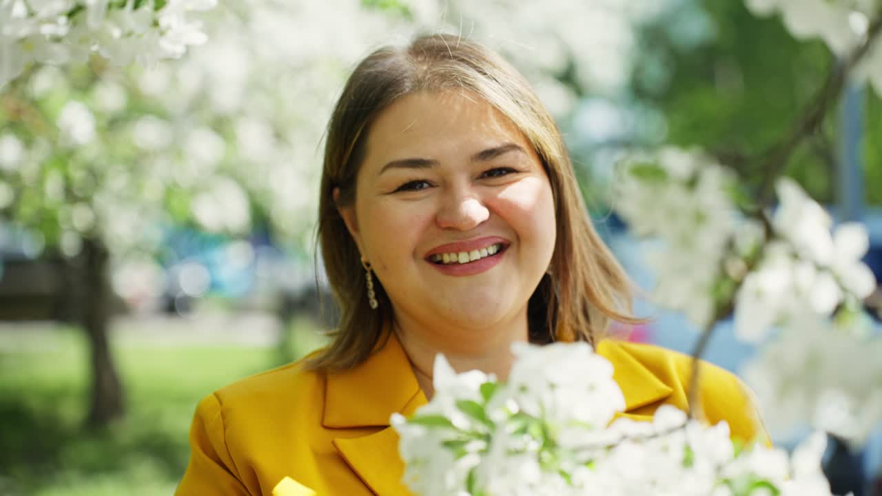 Smiling woman in a yellow jacket, surrounded by spring flowers