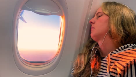 woman sleeping on plane during golden hour, listening to music on airplane