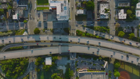 Birds-eye-shot-of-traffic-on-multilane-highway-elevated-above-building-in-city-borough.-Low-sun-casting-long-shadows.-Miami,-USA